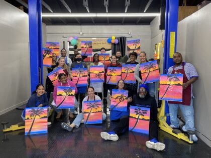 Group holding sunset palm tree paintings at a painting class.